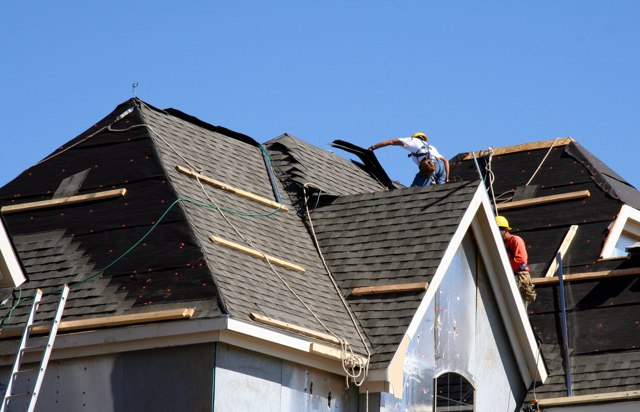 Construction workers putting shingles on the roof of a house