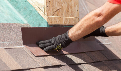Roofer builder worker installing shingles on a new wooden roof with skylight