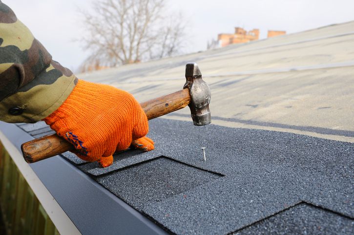 Worker hands installing bitumen roof shingles. Worker Hammer in Nails on the Roof. Roofer is hammering a Nail in the Roof Shingles. Construction Nails Vapor barrier and Waterproofing. Unfinished roof.
