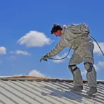 A trademan uses an airless spray to paint the roof of a building