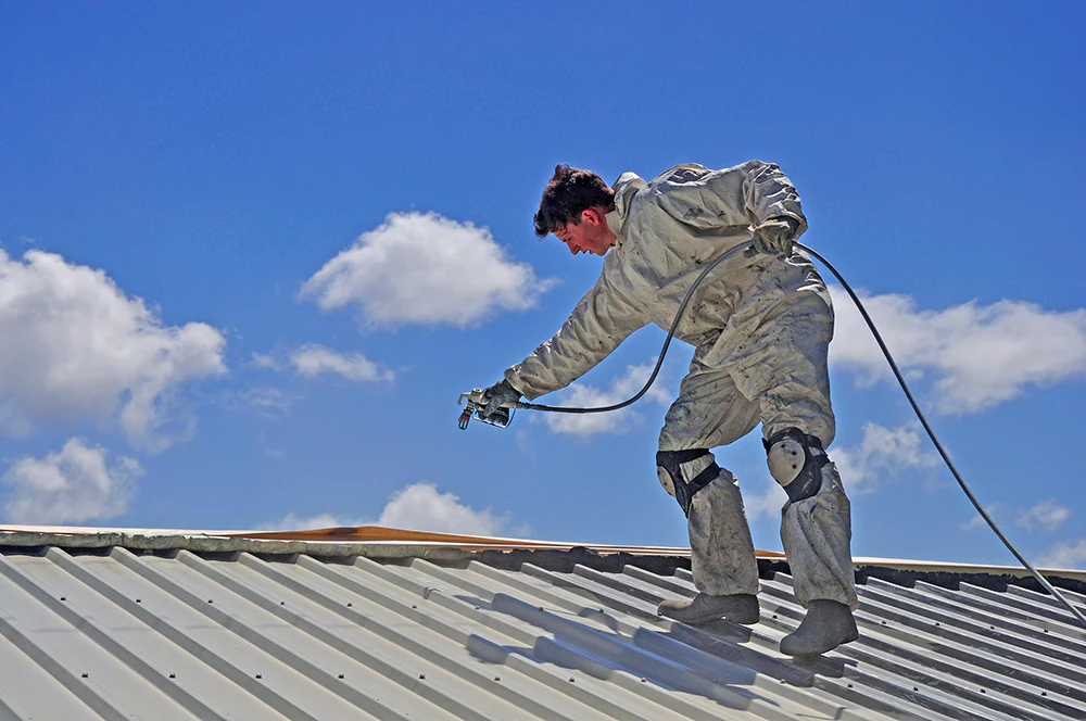 A trademan uses an airless spray to paint the roof of a building